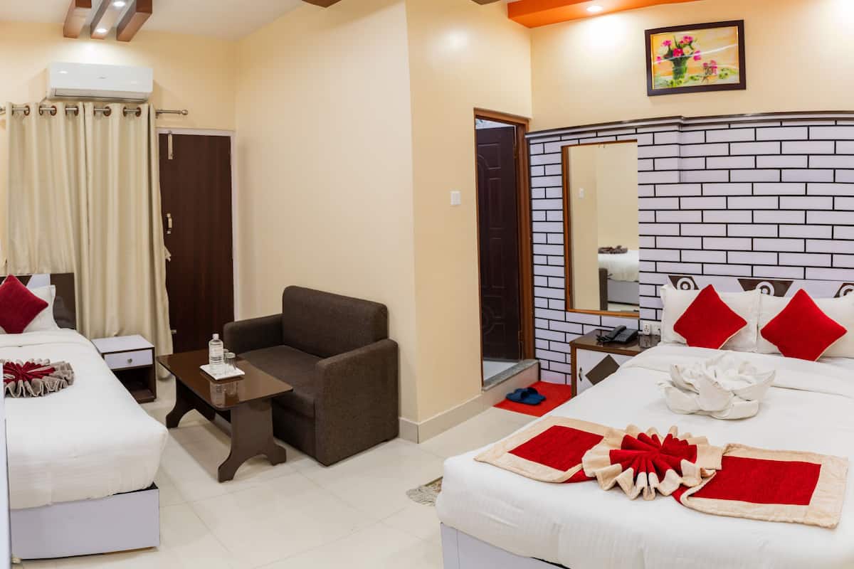 A hotel room with two beds, a sofa, a small table, a TV, and a bathroom door.