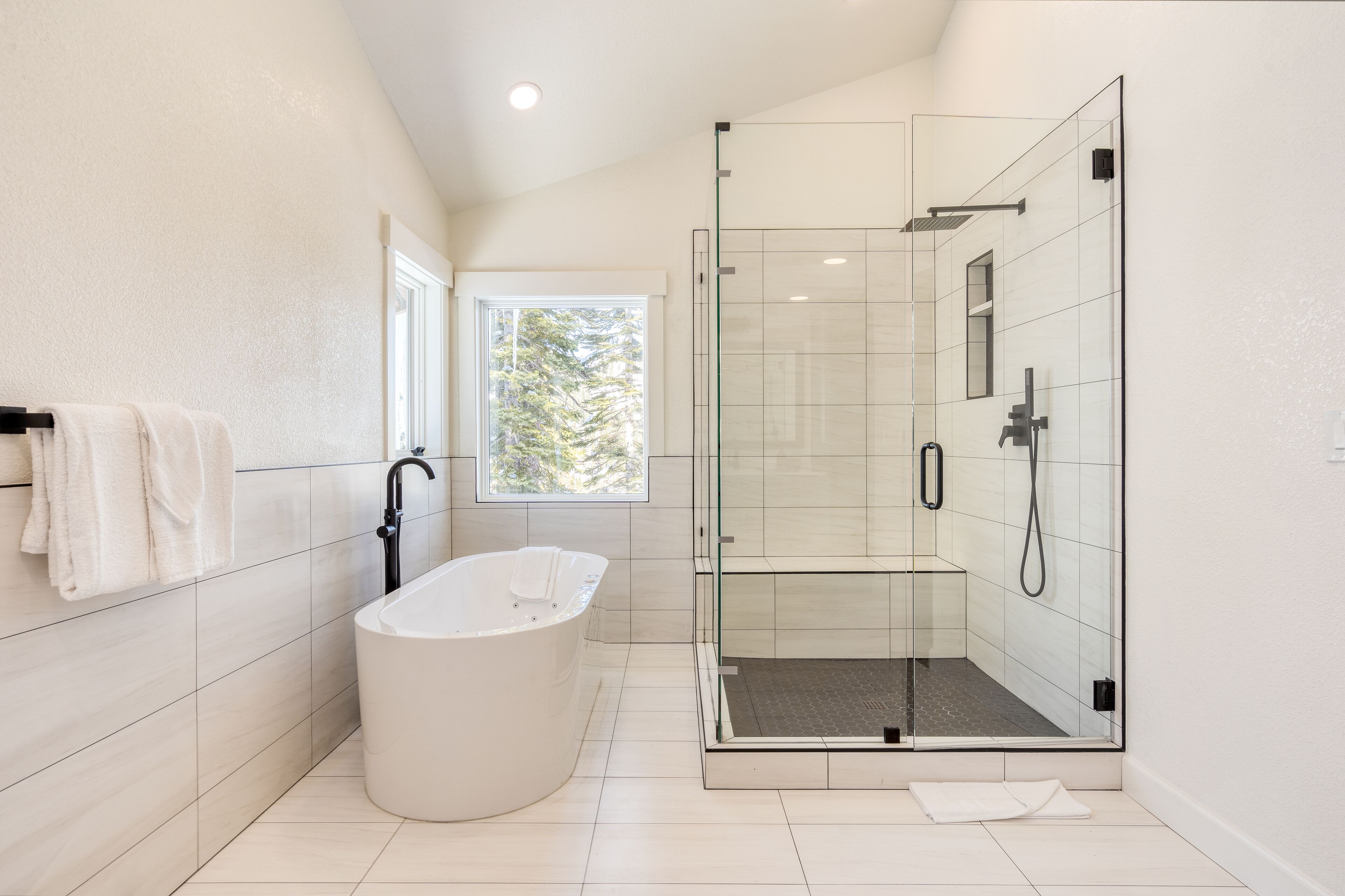 Une salle de bain moderne avec une baignoire sur pieds, une douche à parois de verre et une fenêtre laissant entrer la lumière naturelle.