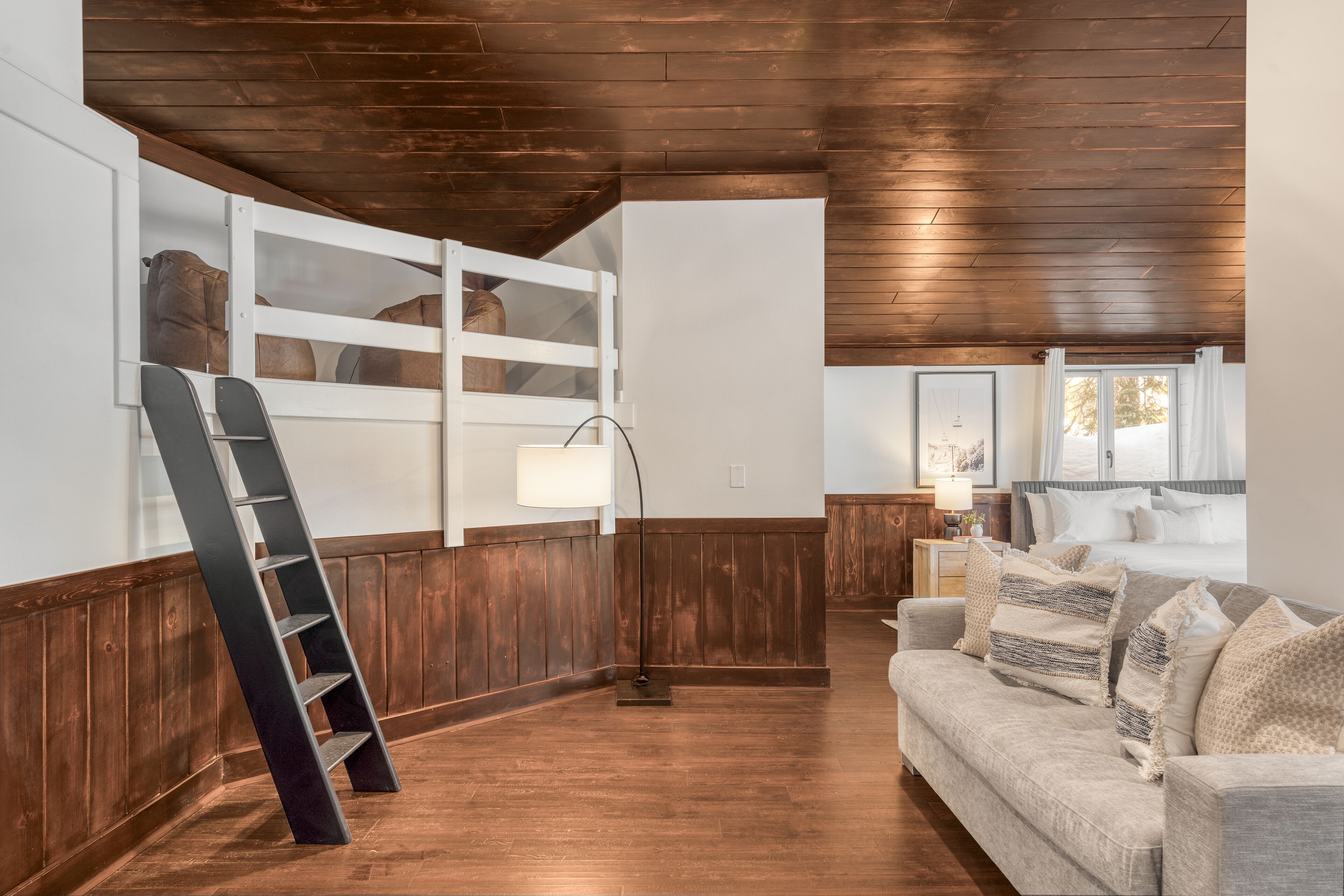 Una habitación con techo de madera, un mueble blanco con espacio de almacenamiento, un sofá con cojines y una escalera.