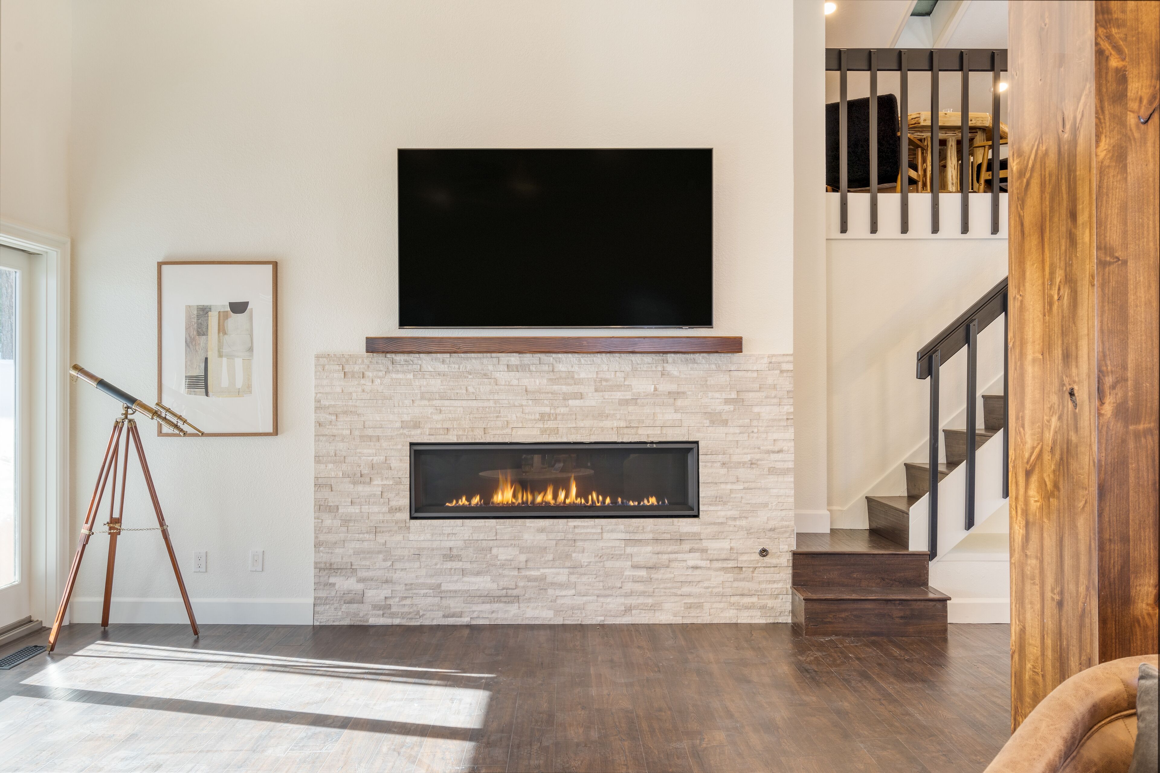 A modern living room with a fireplace, a mounted TV, and a staircase.