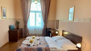 A hotel room with a bed, bedside tables, a desk, a chair, a potted plant, and a window with curtains. - Hotel Victor  (Prague)