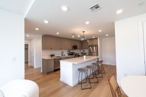 Una cocina moderna con una isla central, taburetes de bar y electrodomésticos de acero inoxidable.