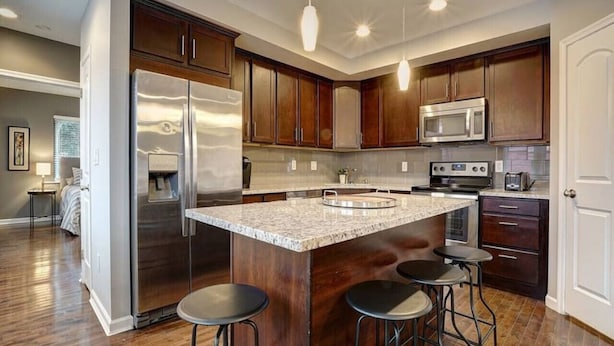 Una cocina moderna con una isla central, electrodomésticos de acero inoxidable, armarios de madera oscura y una zona con taburetes de bar.