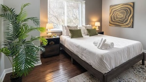 Un dormitorio con cama, mesitas de noche, lámparas, un ventanal grande y una planta en maceta.