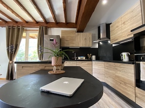 A modern kitchen with a round black table, a laptop, wooden cabinets, and a potted plant.