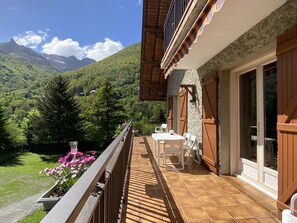 A balcony with a table and chairs, overlooking a mountainous landscape with greenery and a clear sky. - Vaste T4 115m2. Balcon. Vue. Suite. Jardin et jeux (Cauterets)
