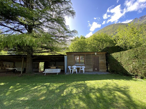 A rustic wooden cabin with a covered patio, two white plastic chairs, and a table.