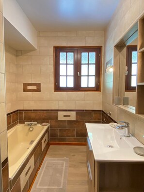 A modern bathroom with a double sink, a bathtub, and a window with frosted glass panes. - Vaste T4 115m2. Balcon. Vue. Suite. Jardin et jeux (Cauterets)