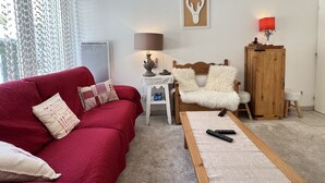 Ein rotes Sofa mit gemusterten Kissen, ein Couchtisch aus Holz, eine Lampe, ein gerahmtes Bild und ein Schrank mit einer roten Lampe.
