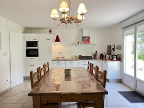A modern kitchen with white cabinetry, a dining table, and a chandelier. - La maison de FanloU (Cauterets)