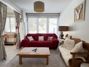 A living room with a red sofa, a wooden coffee table, a white furry sofa, a lamp, and a framed antler decoration.