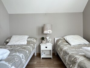 A bedroom with two beds, a nightstand with a lamp, and a small shelf. - La maison de FanloU (Cauterets)