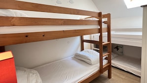 Dormitorio con literas, una escalera de madera, ropa de cama blanca y un mural con diseño de luna y estrellas.