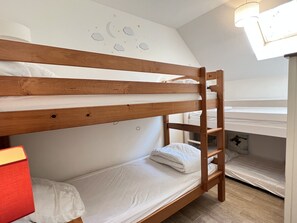 Dormitorio con literas, una escalera de madera, ropa de cama blanca y un mural con diseño de luna y estrellas.