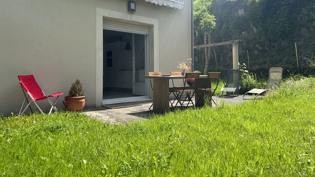 Ein Haus mit einer Terrassenfläche, einem roten Klappstuhl, einem Tisch mit Stühlen und einem Blumentopf.
