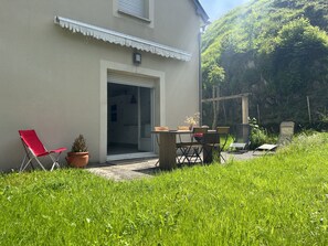 Una casa con un patio, una silla plegable roja, una mesa con sillas y una planta en maceta.