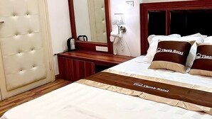 A hotel room with a large bed, a wooden headboard, a mirror, a bedside table, and a wall-mounted artwork. - GRAD Dai Thanh Motel (Hanoi)