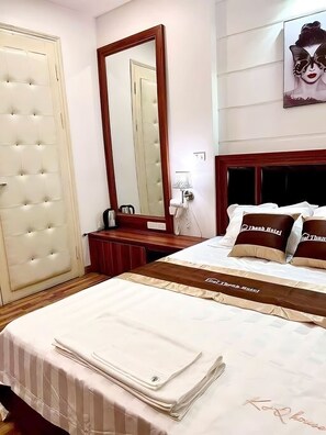 Habitación de hotel con una cama grande, un cabecero de madera, un espejo, una mesita de noche y una obra de arte colgada en la pared.