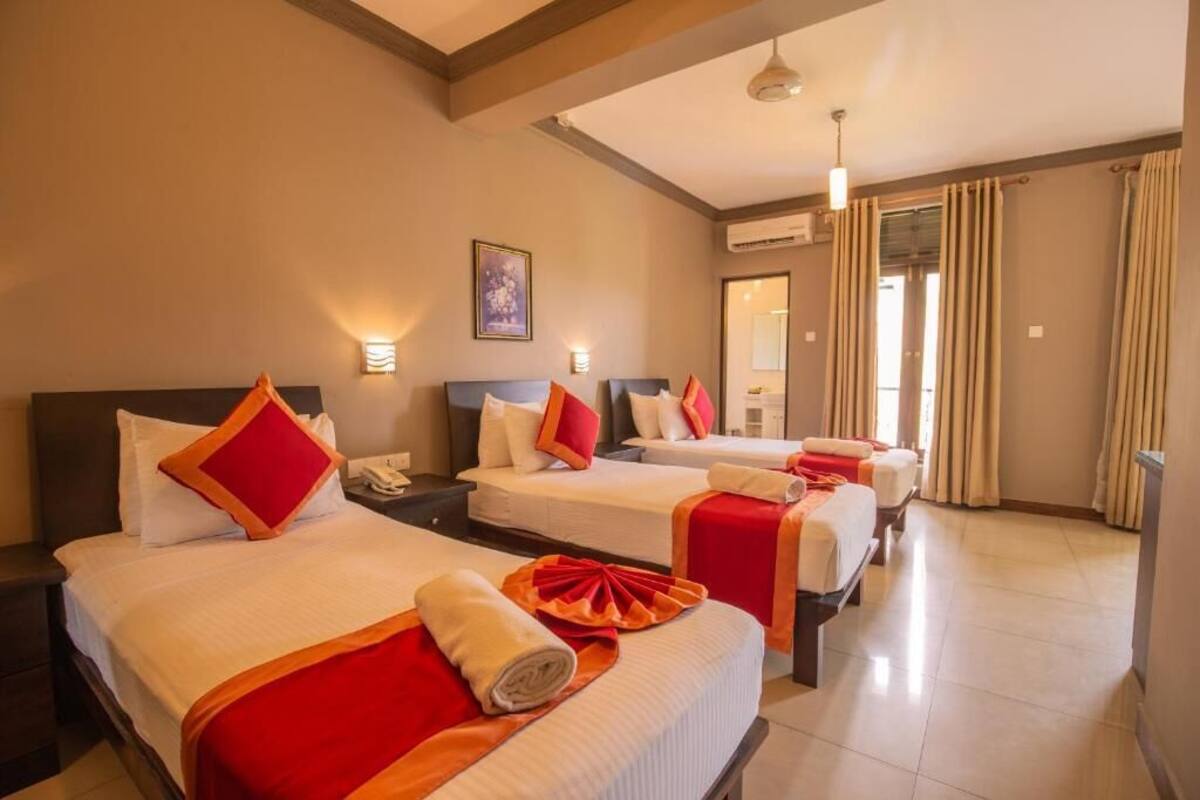 A hotel room with three beds, each with red and white bedding, a large mirror, and a ceiling fan.