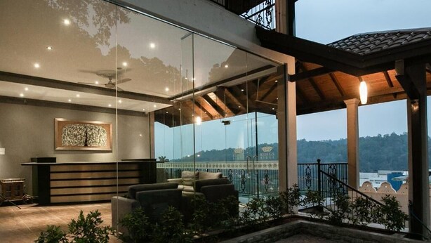 Un espacio exterior moderno con pared de vidrio, terraza de madera y vistas a un paisaje montañoso.