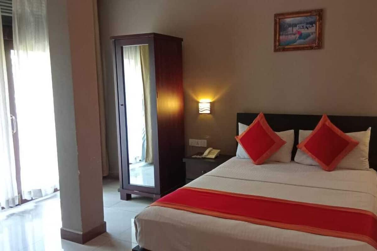 A hotel room with a bed, two bedside lamps, a nightstand, a wardrobe, and a painting on the wall.