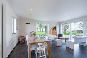 A spacious living area with a dining table, white sofas, and a view of a garden through large windows. - Spacious Holiday Home with Pond (Roesbrugge)