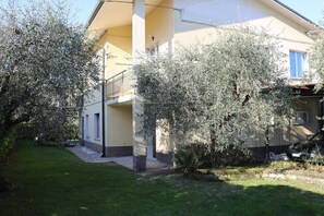 A two-story building with a balcony, a garden with olive trees, and a parked car. - Lazise Serene Garden Escape (Lazise)