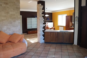 A modern kitchen with a central island, a dining area with a sofa, and a large window providing natural light.