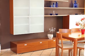 A dining area with a wooden table and chairs, a bench, and a cabinet with shelves above.
