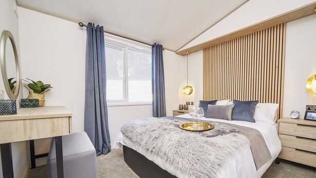A modern bedroom with a bed, bedside tables, a desk, a mirror, and a window with curtains. - Atlas Lilac Lodge VIP (Moortown)