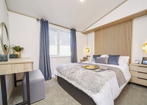 Ein modernes Schlafzimmer mit Bett, Nachttischen, Schreibtisch, Spiegel und einem Fenster mit Vorhängen.