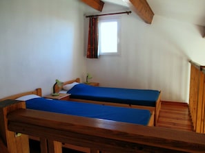 A room with two wooden beds, a window with curtains, and a wooden ceiling.