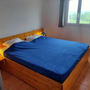 A single bed with a wooden headboard, a blue bedspread, and a bedside lamp.