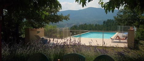 Une piscine avec vue sur les montagnes, entourée d’une clôture et de verdure.