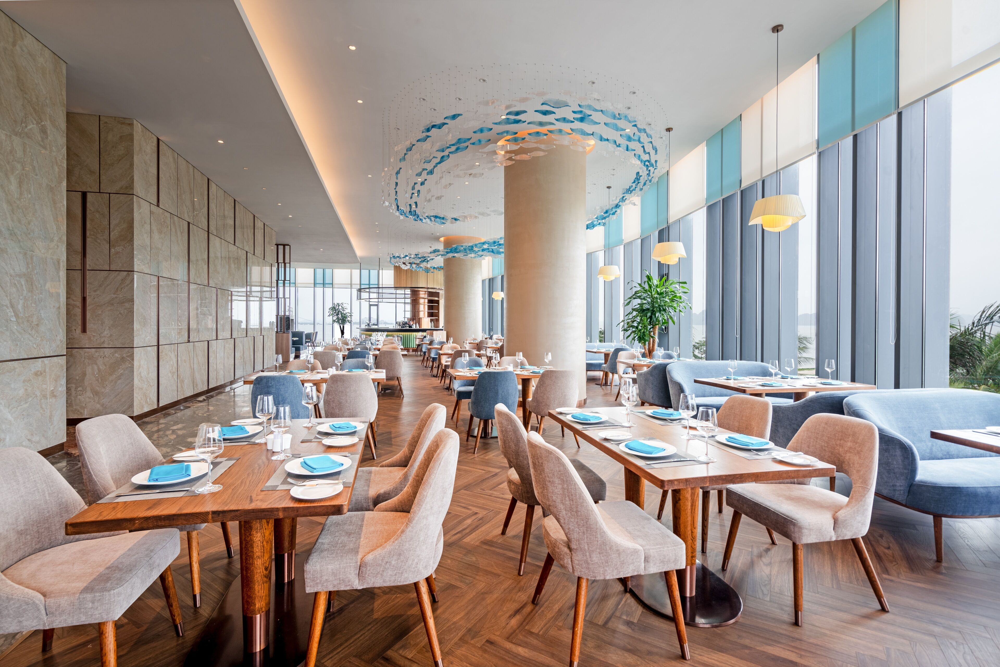 A spacious restaurant with high ceilings, modern furniture, and large windows offering views of the city.