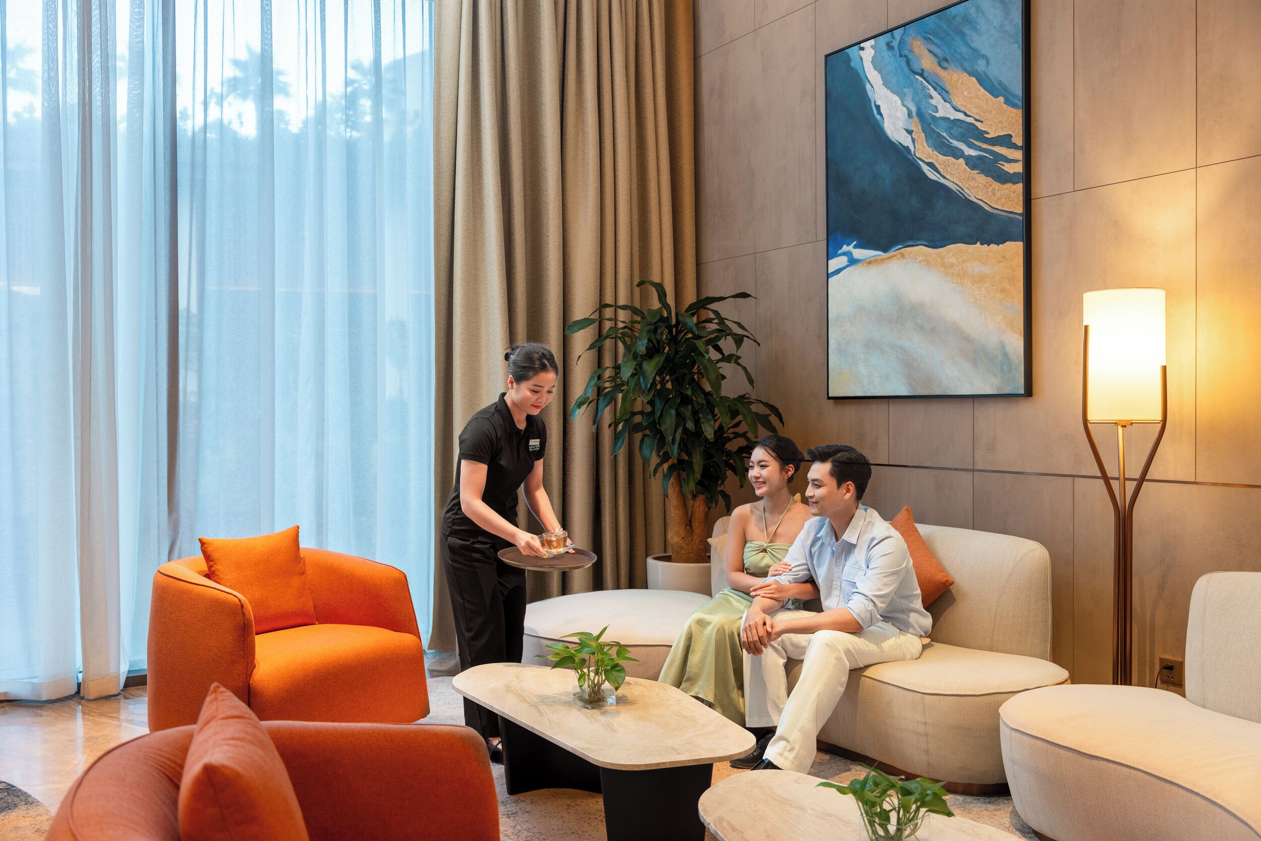 A modern hotel lobby with a seating area, a large painting, and a floor lamp.