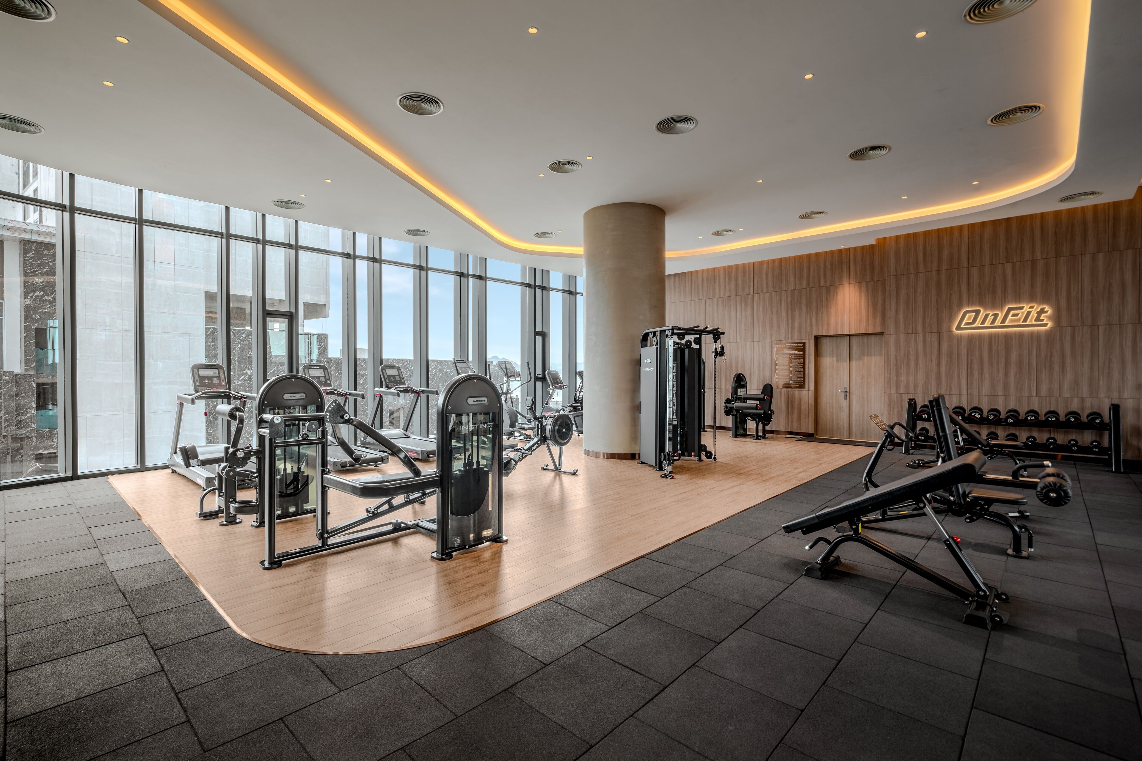 A modern gym with cardio machines, free weights, and a large window offering a city view.