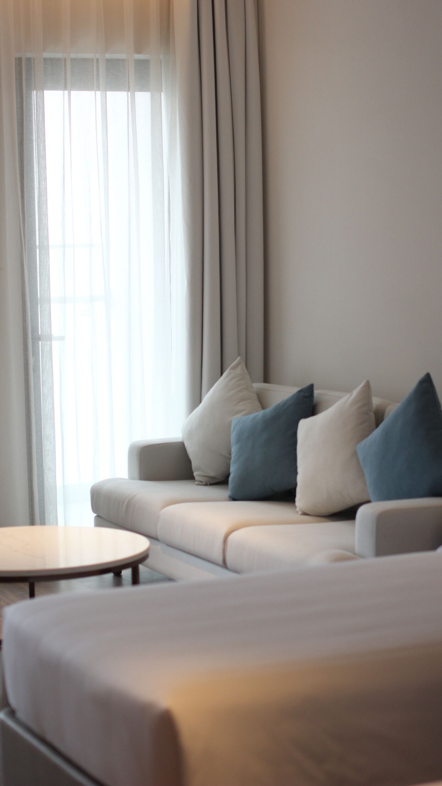 A modern living room with a sofa, a coffee table, and a large window with sheer curtains.