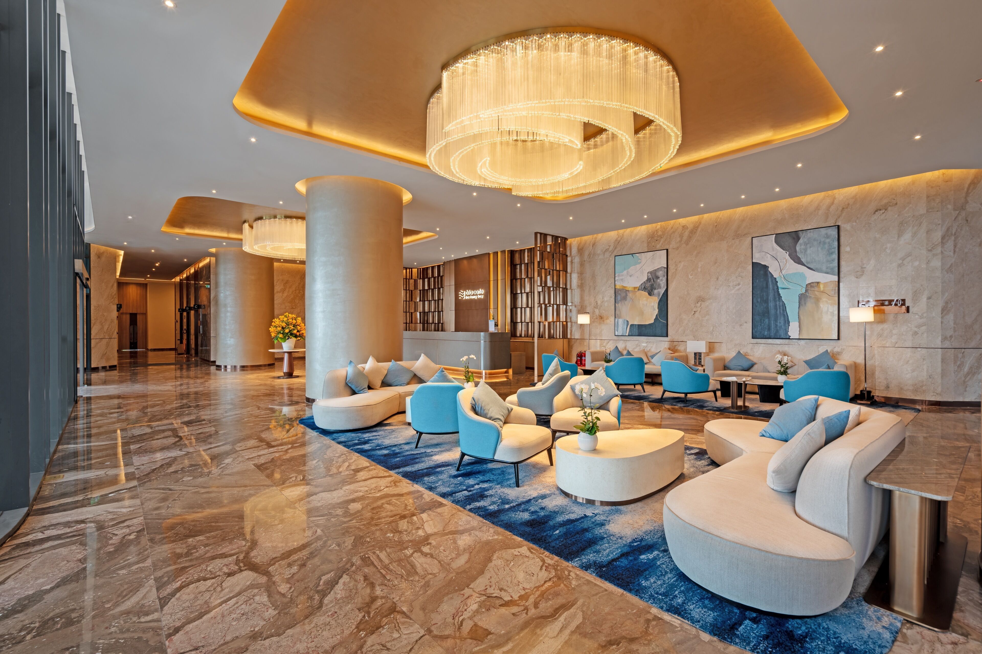 A modern lobby with a marble floor, blue and white sofas, a large chandelier, and a reception desk.