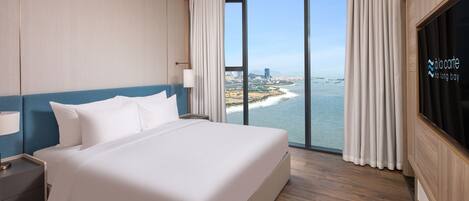 A hotel room with a large bed, a TV, and a view of the ocean and cityscape.