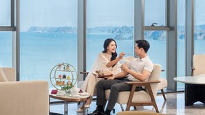 Una habitación moderna con ventanas amplias, una mesa redonda y un atril decorativo con objetos.
