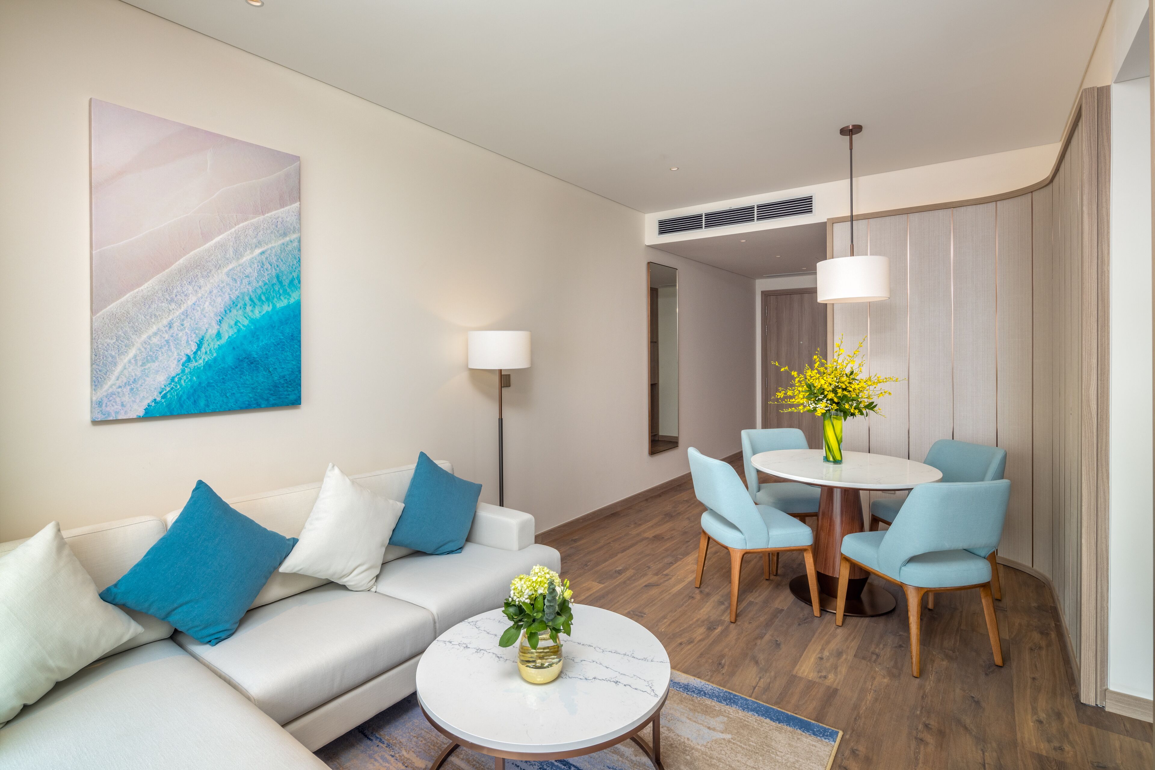 A modern living room with a sofa, a coffee table with a vase, and a dining area with chairs and a table.
