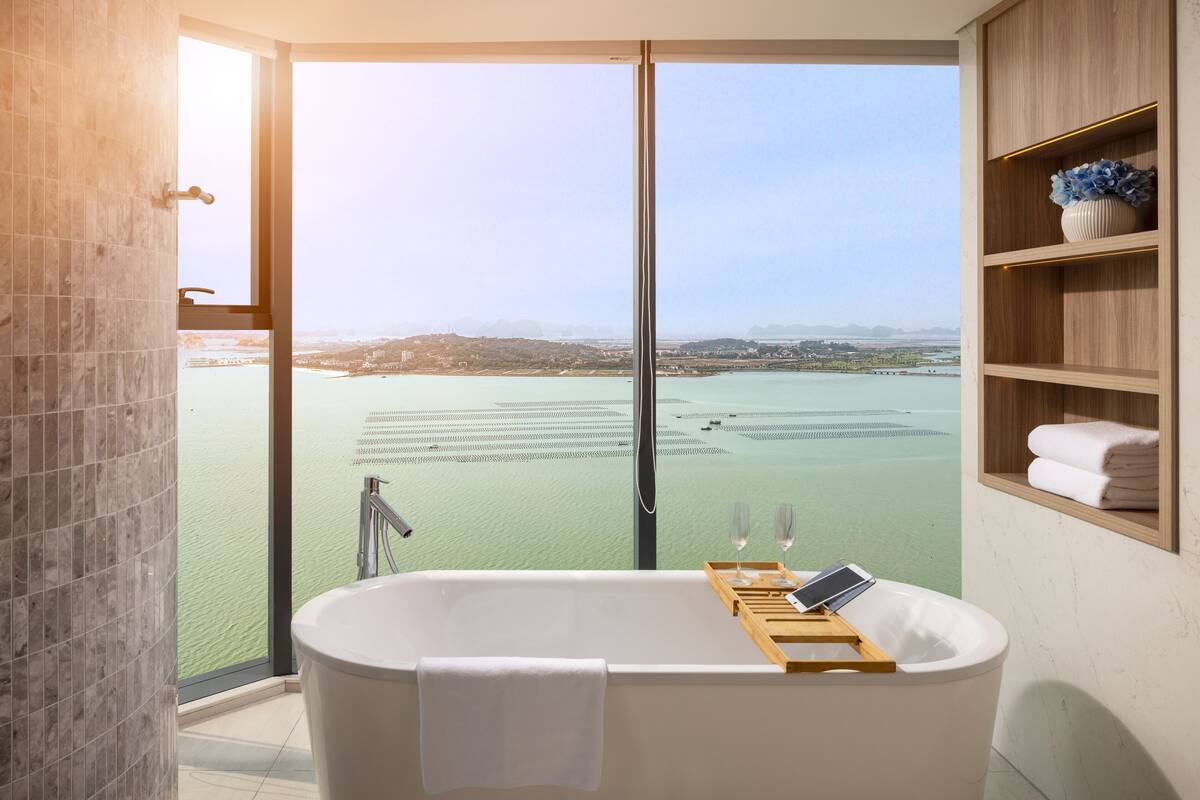 A modern bathroom with a large bathtub, a glass shower enclosure, and a view of a body of water.