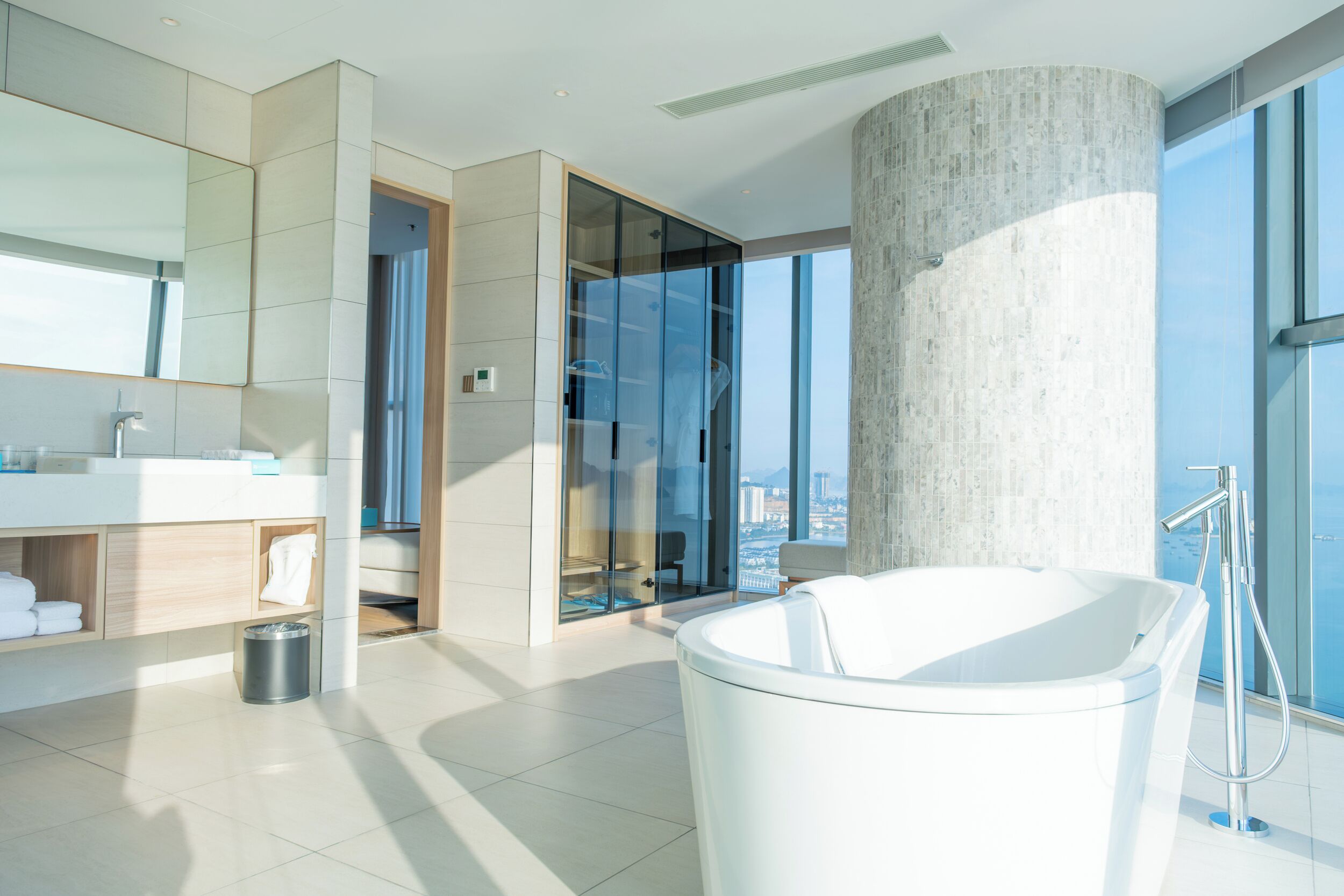A modern bathroom with a large bathtub, a glass-enclosed shower, and a city view.