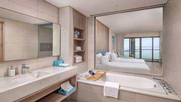A modern bathroom with a large mirror, two sinks, a bathtub, and a view of a bedroom with a balcony.