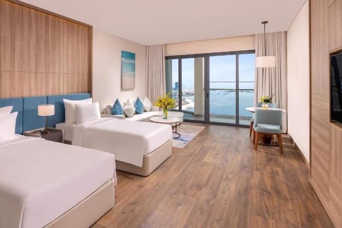A hotel room with two beds, a sofa, a dining table, and a TV.