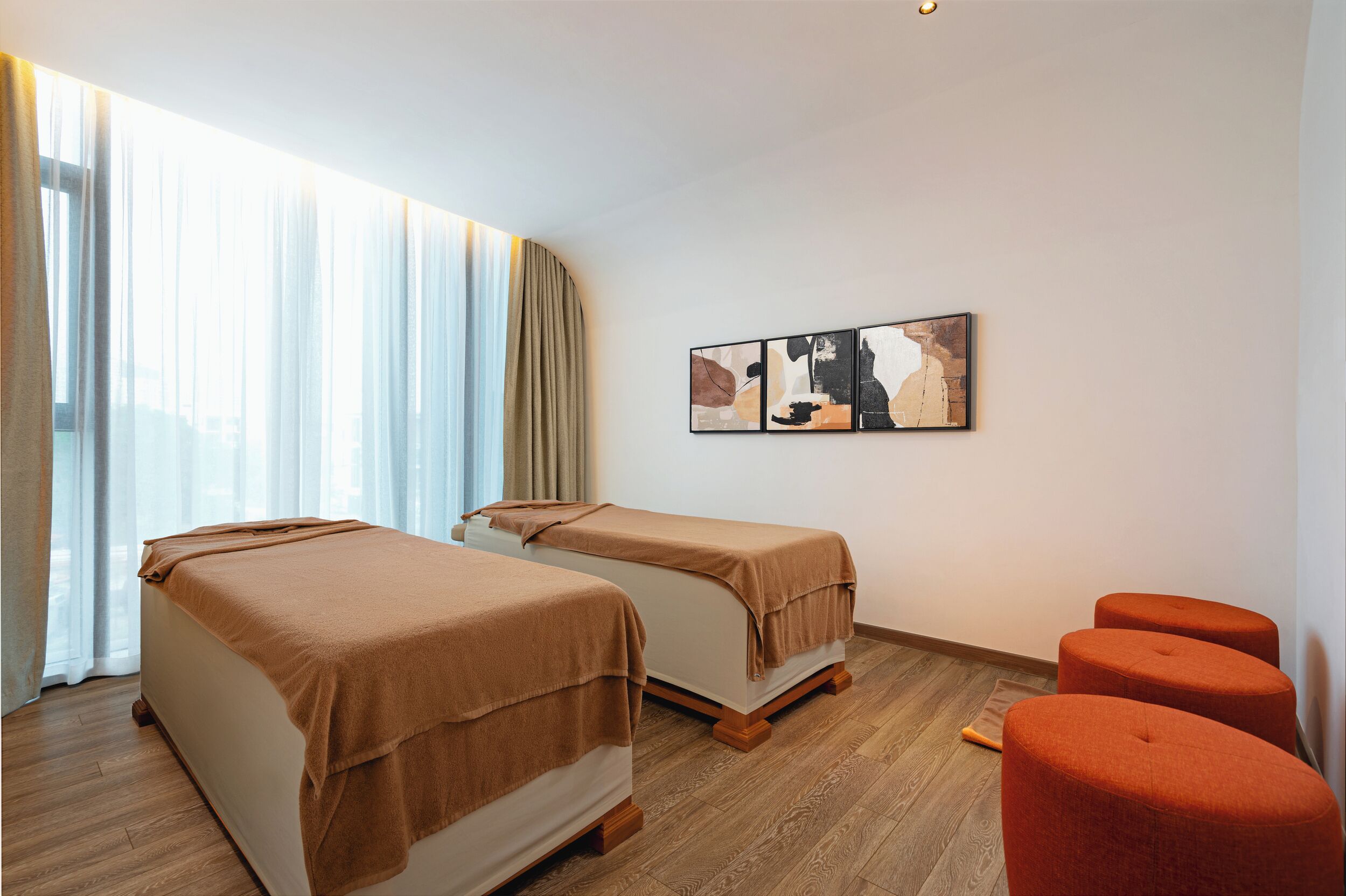 Une chambre d’hôtel avec deux lits, une grande fenêtre avec des rideaux légers, une œuvre d’art accrochée au mur et un plancher en bois.