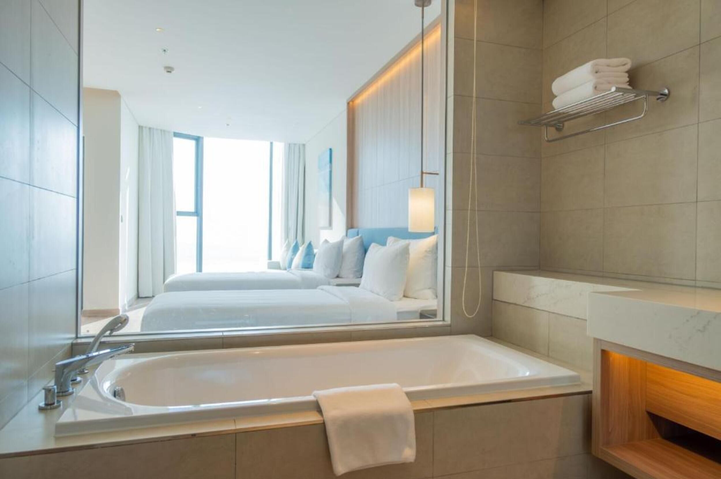 A modern hotel bathroom with a large bathtub, a mirror, and a towel rack.