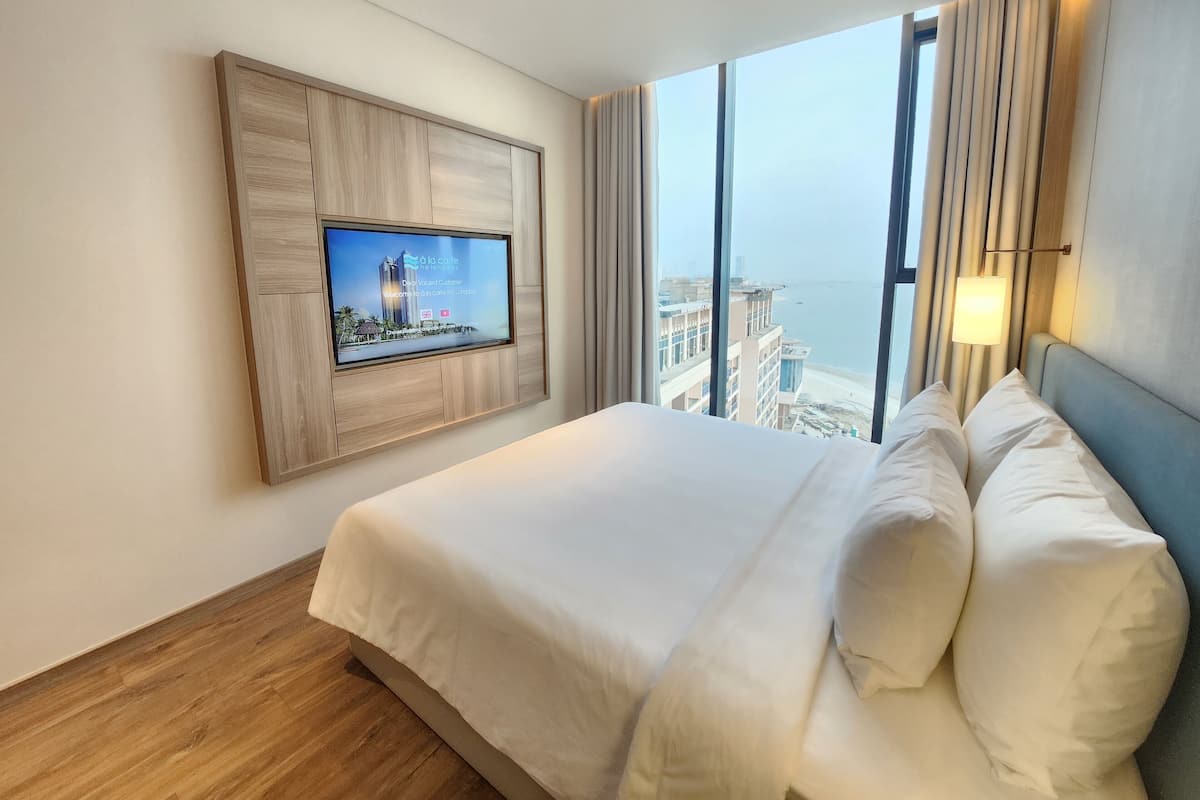 A hotel room with a large bed, a TV mounted on the wall, a view of the city, and a window with curtains.