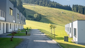 A row of modern, single-story buildings with a paved driveway leading to a grassy area.